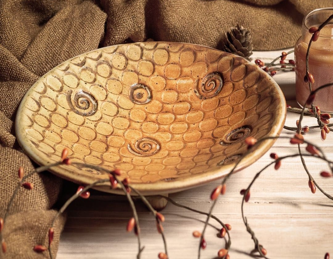 A bowl with a pattern on it sitting next to some branches.