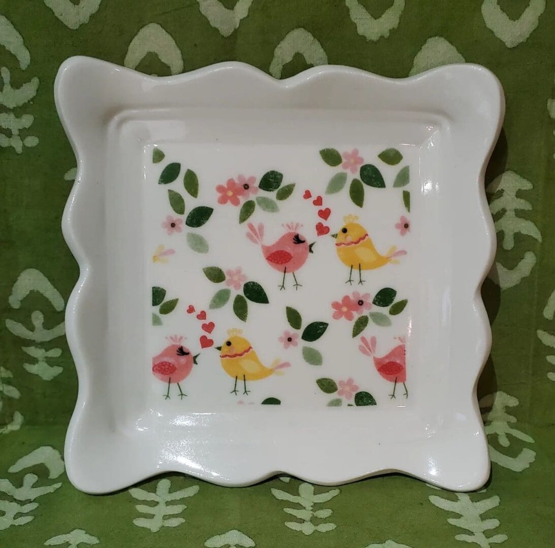 A white square plate with birds and flowers on it.